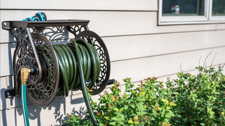 Green garden hose on metal reel attached to vinyl siding