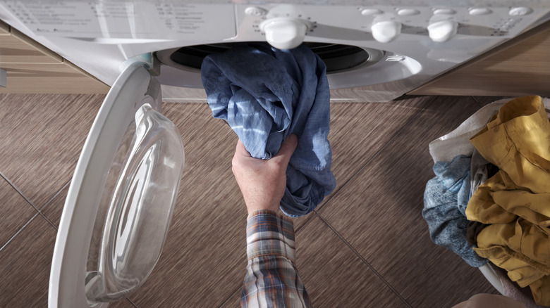 A person throws clothes into the washing machine