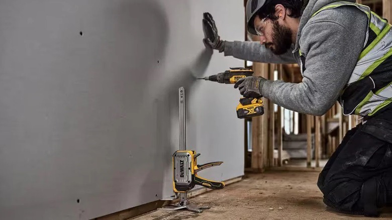 Man holding a drywall sheet with a construction jack before screwing it to the wall