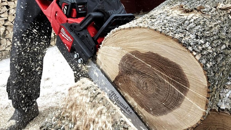 Person cutting a large log with a Milwaukee chainsaw