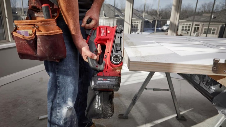 Person using a portable belt sander on a door