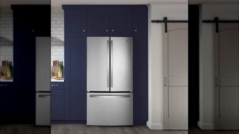 A french door style GE refrigerator is displayed in a kitchen with navy blue cabinets and subway tile backsplash