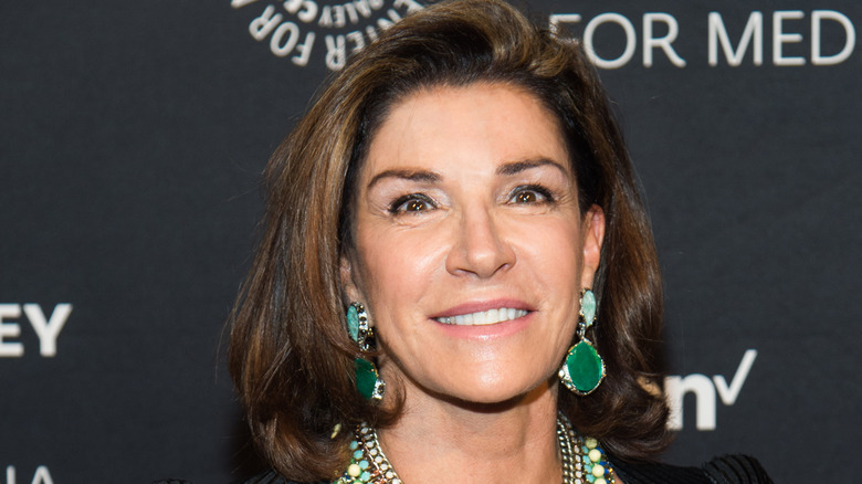 Hilary Farr smiling in pink lipstick and green earrings.