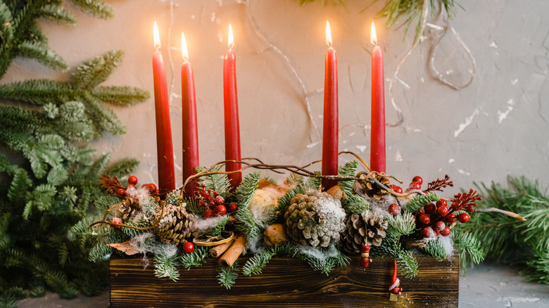 Greenery nestles in a wooden tray, topped with red candles