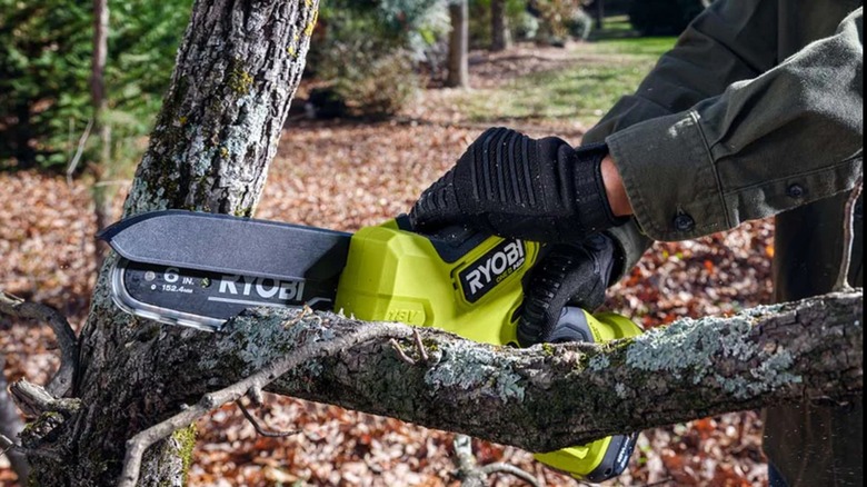 A person cutting a tree branch with a Ryobi mini chainsaw