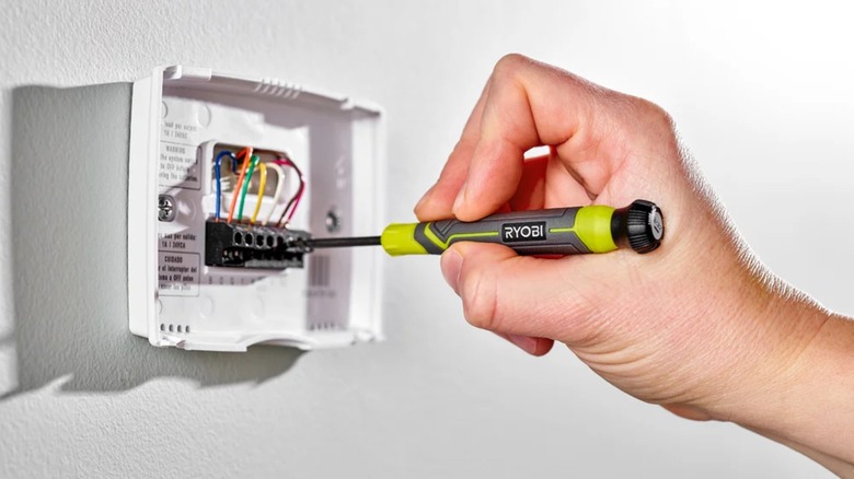 A person using a precision screwdriver to fix a thermostat