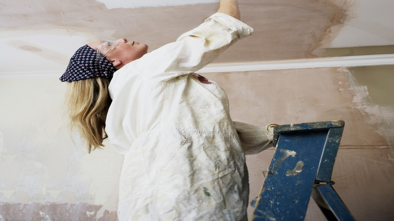 Woman standing on a step ladder painting her home's ceiling