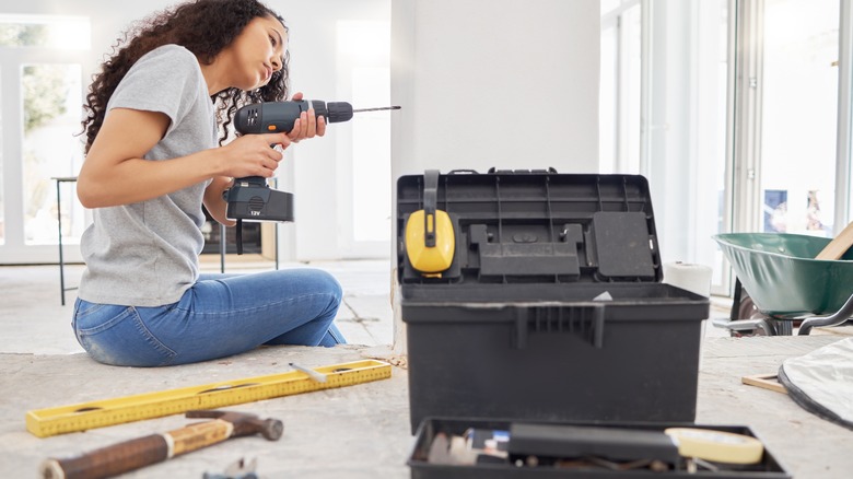 Woman doing a home project, holding a drill with a tool box at her side