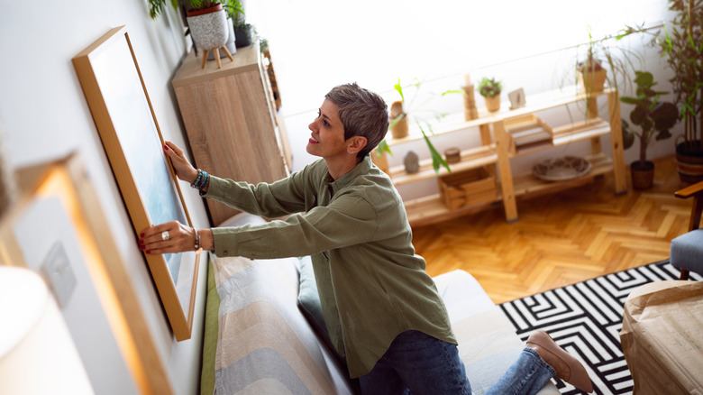 A woman adjusting the art on her living room wall