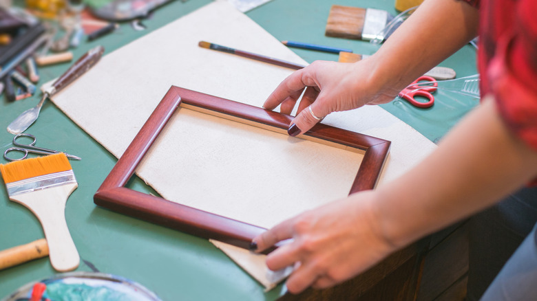 A pair of women's hands arrange supplies to customize a picture frame.