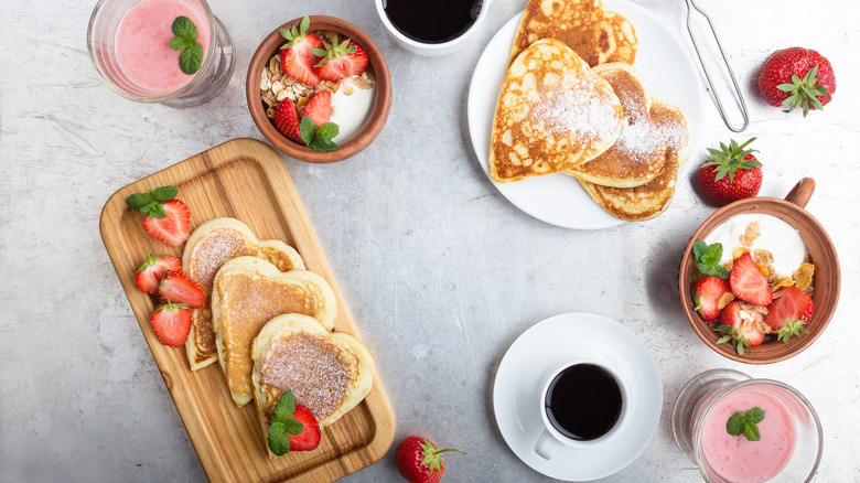 A breakfast with coffee, heart-shaped pancakes and strawberries sits on the desk.