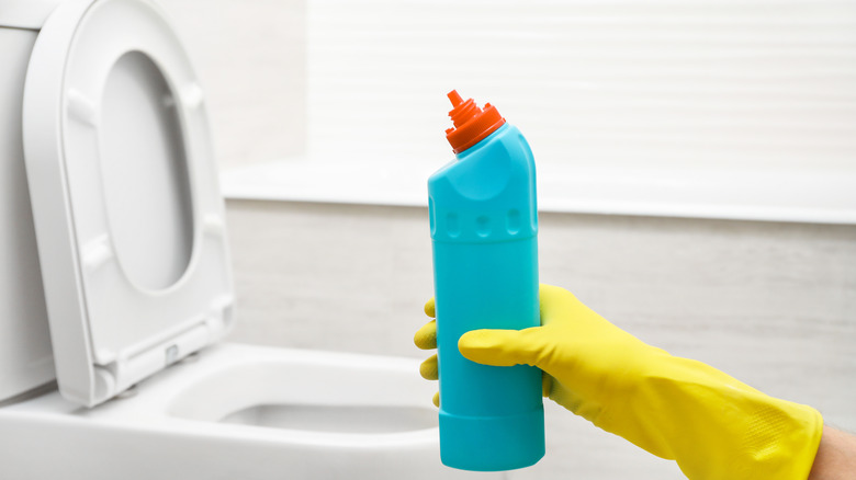 gloved hand holding toilet cleaner 