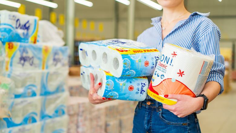 A woman holds two large packs of toilet paper