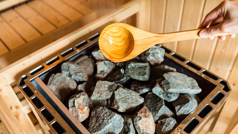 Wooden ladle pouring water onto sauna rocks
