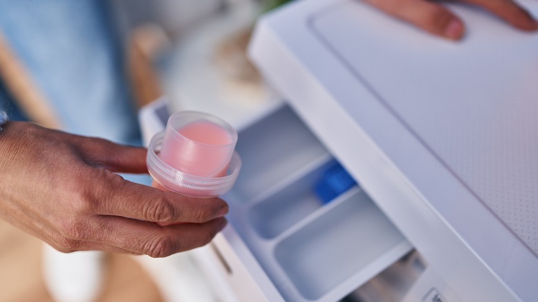 Person pouring cap full of pink detergent into washing machine compartment