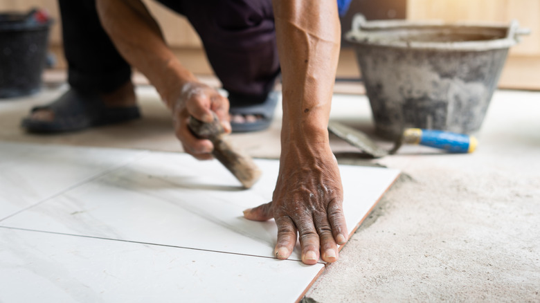 A person's hands installing a tile floor