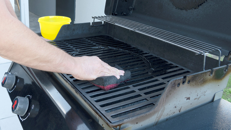 Man cleaning grill with sponge