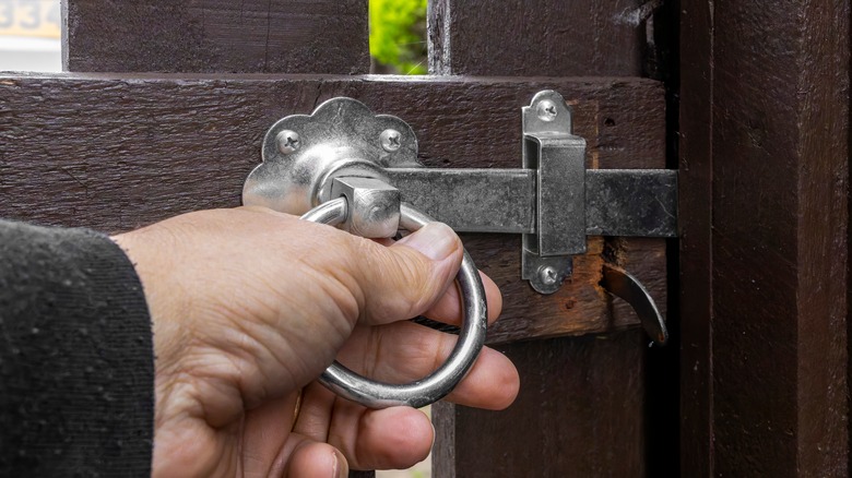 Man holding the ring of a metal gate latch