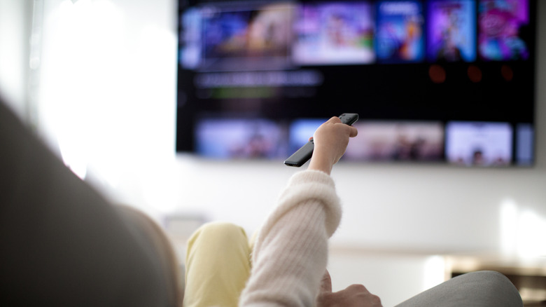 Woman points TV remote towards wall-mounted screen