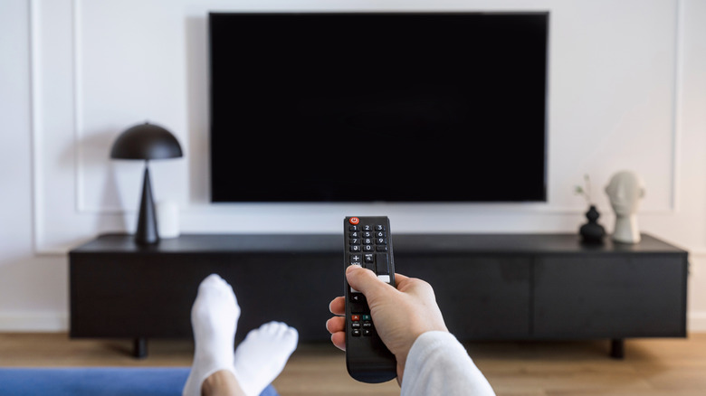 Woman with her feet up holds remote control at TV mounted on wall above black console