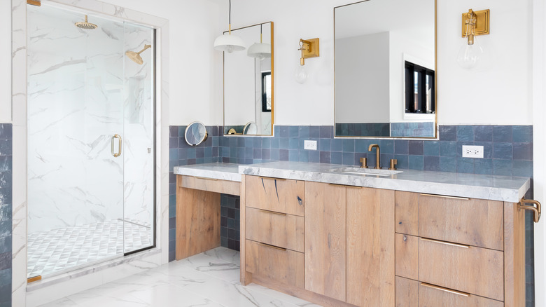 A contemporary bathroom with wooden cabinetry, blue tile, and brass fixtures