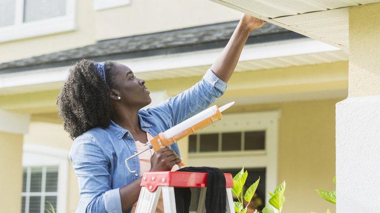 Woman applying caulk to exterior of a house