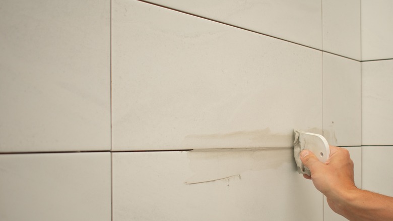 Person grouting shower tiles in bathroom