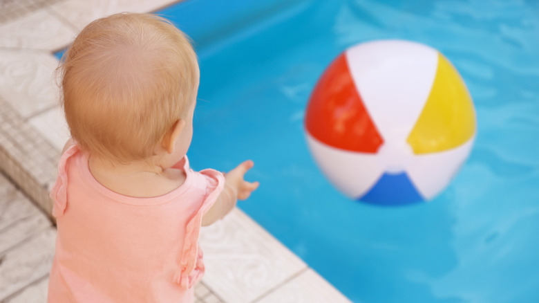 baby reaching for ball in pool