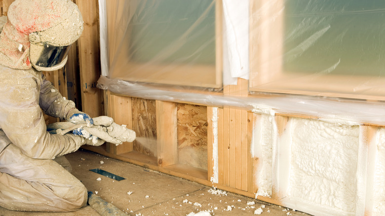 Worker sprays foam insulation under a window in a newly constructed wall