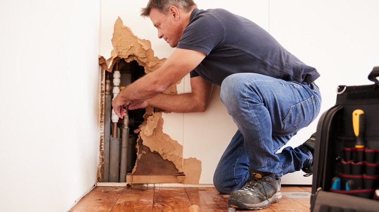 Person repairing pipe behind wall