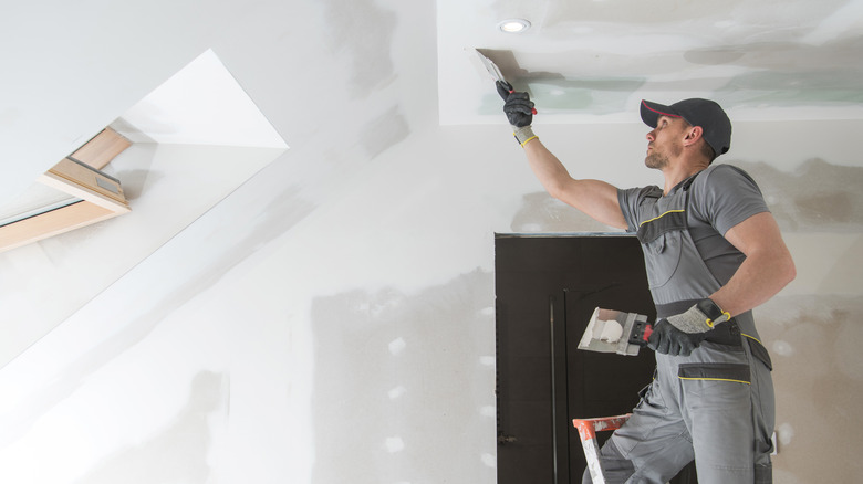 Person mudding drywall on ceiling