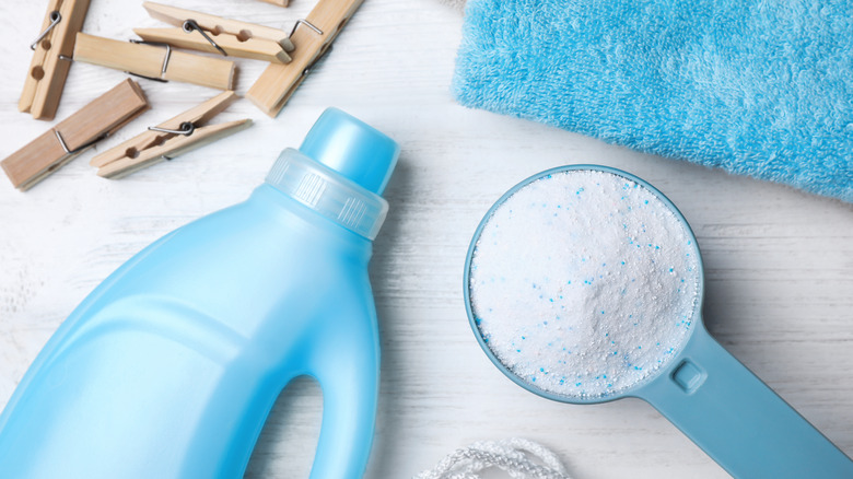 Flat lay composition with laundry detergents, clothespins and towels on white wooden background