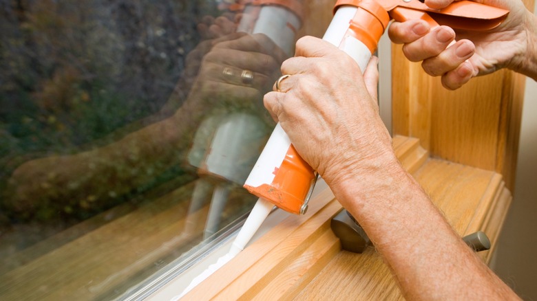 A close up shot of a person applying caulk to windowsill