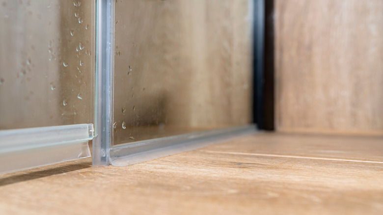 Close up of a glass shower door with water droplets and bottom seal