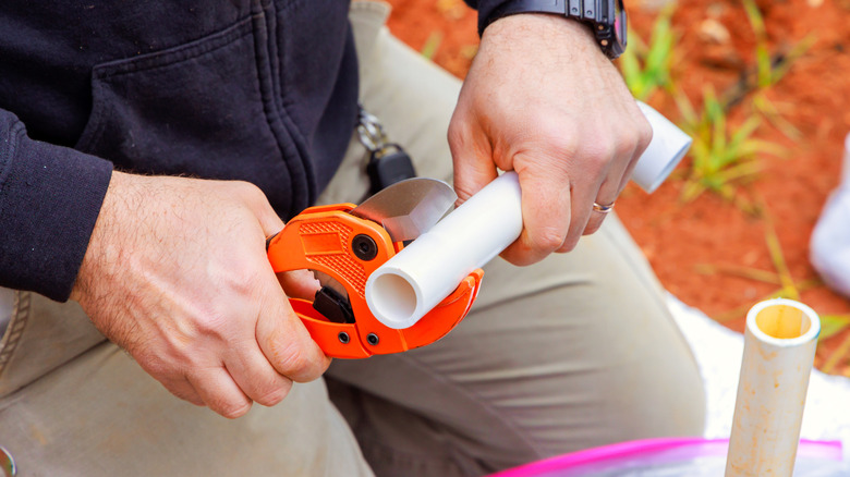 Closeup of the hands of a person using a pipe cutter to cut a PVC pipe