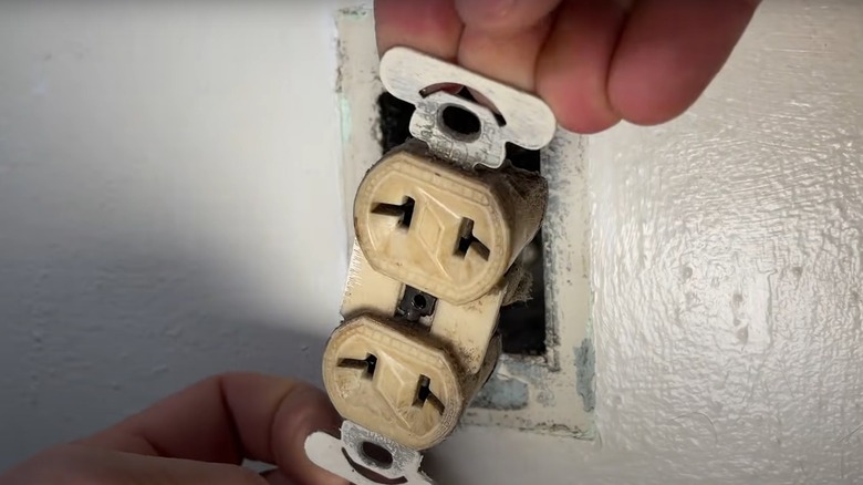 A person removing a two-prong outlet from the wall socket