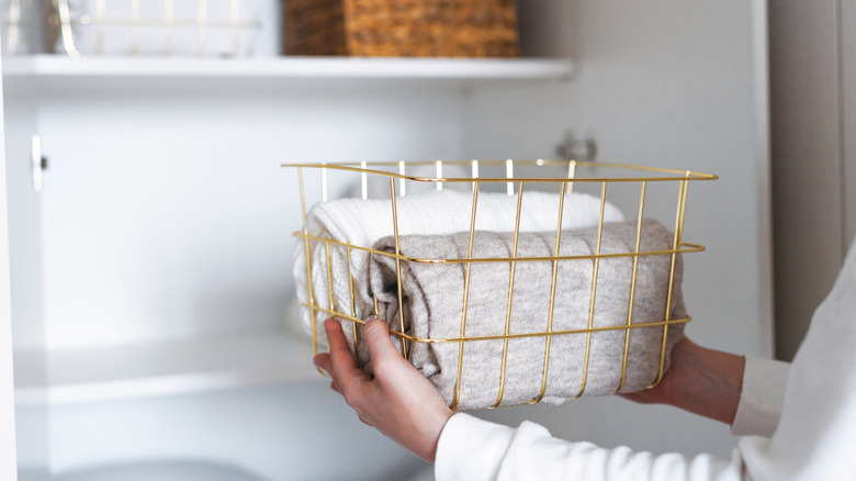 Person placing a gold wire basket with towels on a shelf in their everything closet