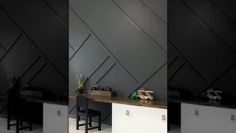 A black accent wall with wooden battens in a diagonal pattern with a white desk with a natural wooden top in front