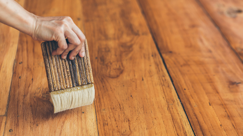 A person applying polyurethane on the hardwood floor