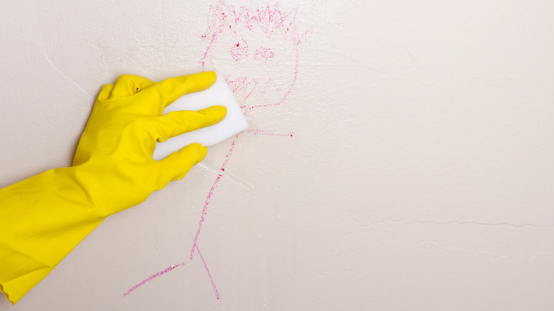 hand with yellow gloves cleaning crayon drawing on wall