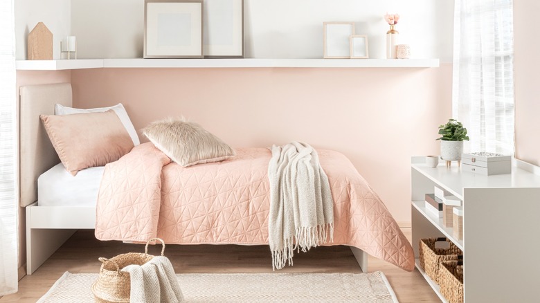 A twin bed in placed under white shelves in a pink bedroom