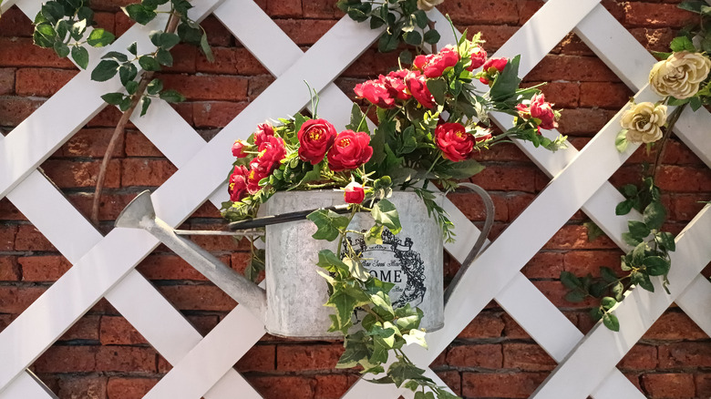 A white trellis with red flowers and other green plants