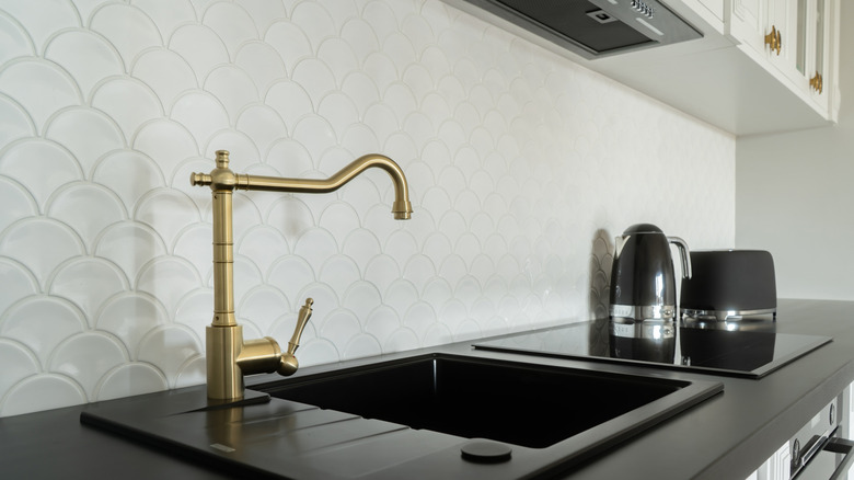 A black kitchen sink and countertop with contrasting white cabinets above