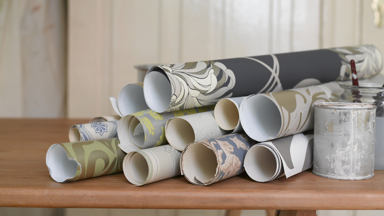 Rolls of wallpaper in different patterns are stacked on a wood table.