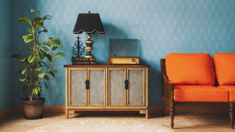 A room is decorated with blue wallpaper and an orange sofa.