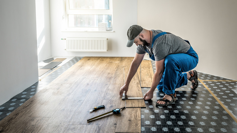 A contractor installs vinyl flooring as the sun streams through the window