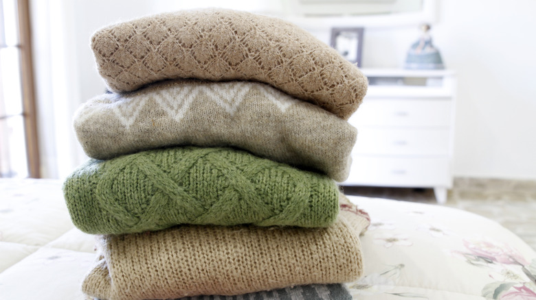 Stack of wool sweaters of various colors on bed