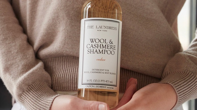 Woman's hands holding a bottle of The Laundress Wool & Cashmere Shampoo