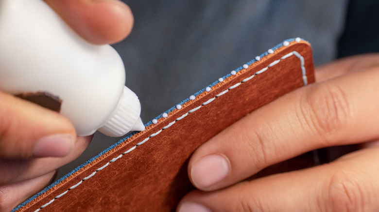 Someone is applying glue to the edge of a leather panel.