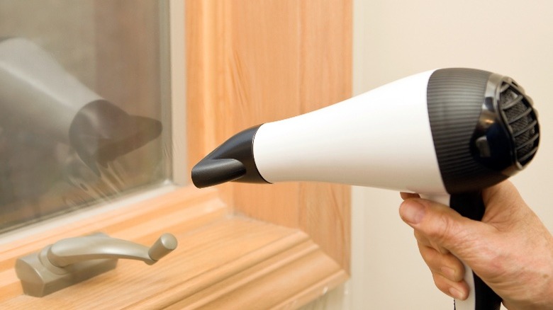 A person uses a hairdryer on window insulation film